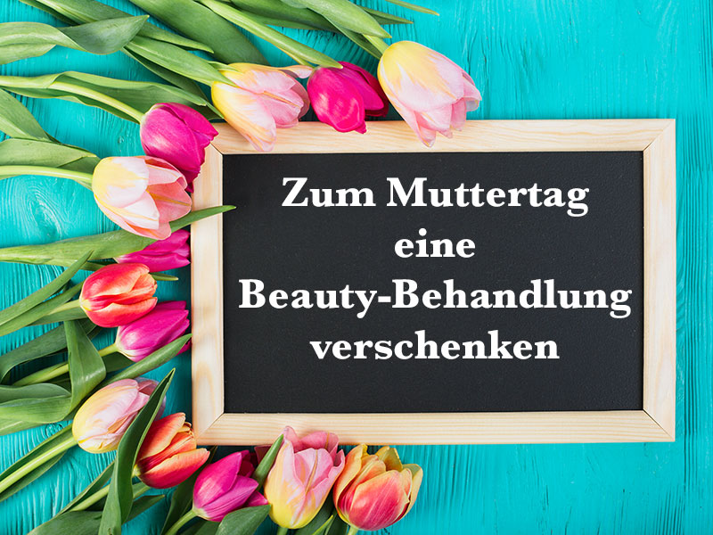 Schiefertafel mit Aufschrift "Zum Muttertag eine Beauty-Behandlung verschenken" umrandet von rosefarbenen Tulpen