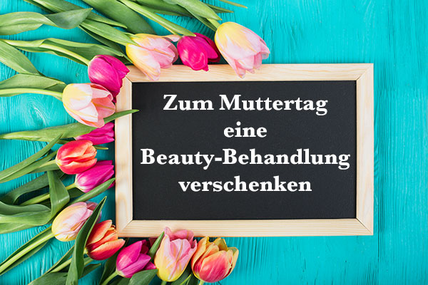 Schiefertafel mit Aufschrift "Zum Muttertag eine Beauty-Behandlung verschenken" umrandet von rosafarbenen Tulpen